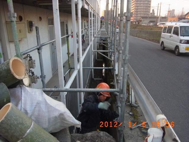 建物と道路のガードレールの間で足場を組む作業
