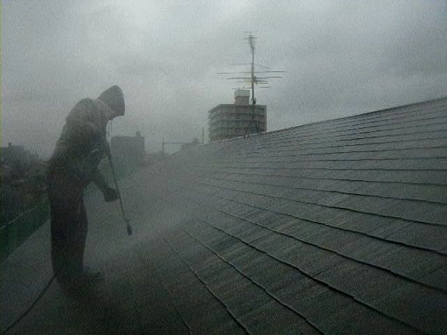 雨の中で南面屋根を高圧洗浄する作業