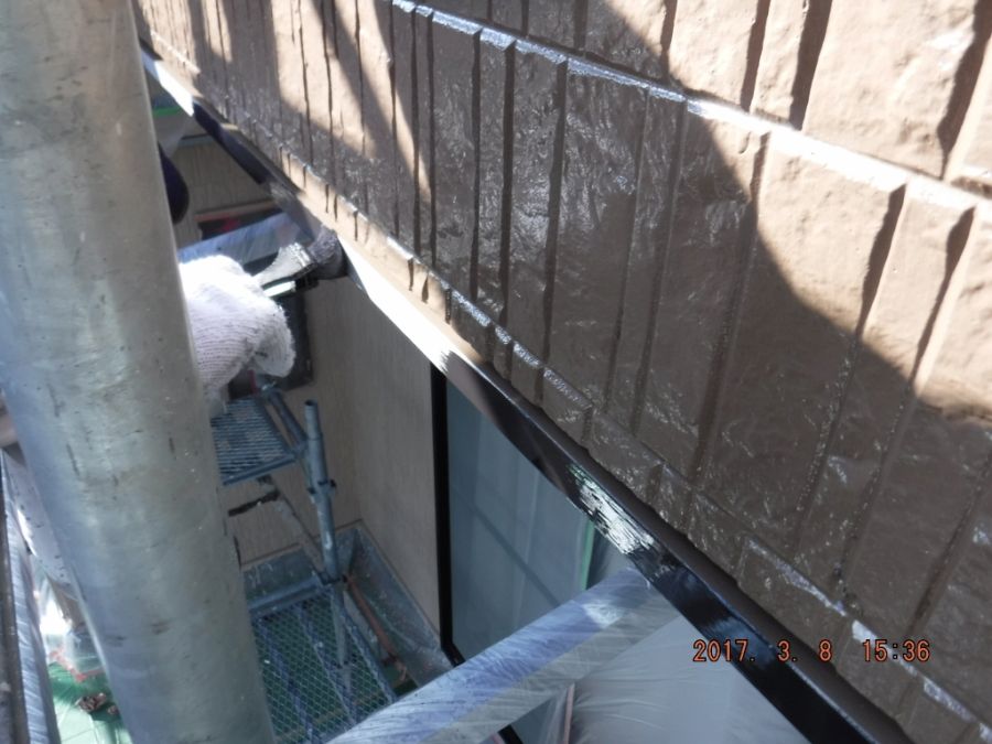 窓上の鉄部に刷毛で上塗りする作業