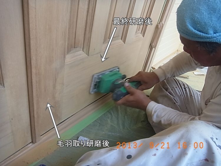 電動サンダーで木製玄関ドアを仕上げ研磨する職人